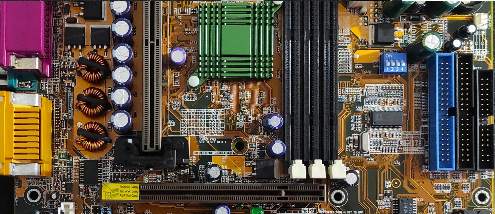 Orange circuit board with green and black components, purple capacitors, yellow connectors, and blue ports.